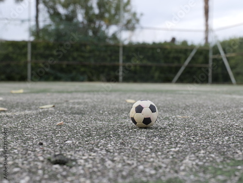 Soccer ball on empty outdoor court ground level view. Sports field with fence and trees in background. Urban recreational area for football training and games.