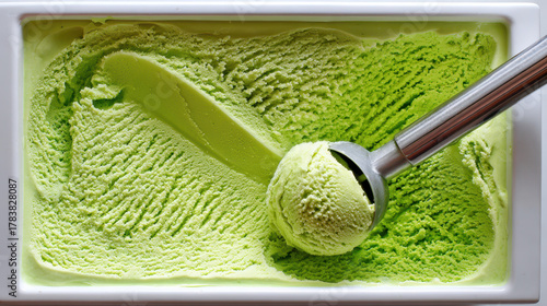 Creamy pistachio ice cream served in a white container with a metal scoop, showcasing a smooth texture and vibrant green color