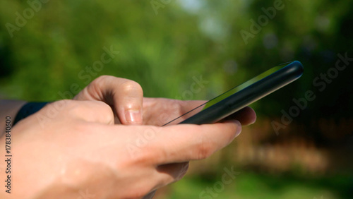 Closeup of man hands using a smartphone outdoors in a sunny garden.