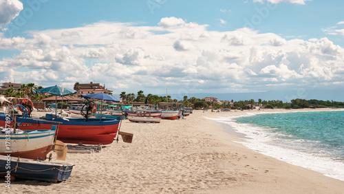 Fototapeta Naklejka Na Ścianę i Meble -  Colorful fishing boats on the sandy beach of Marina di Nicotera, Calabria, Italy, under a bright summer sky. Peaceful coastal scenery and Mediterranean holiday atmosphere.