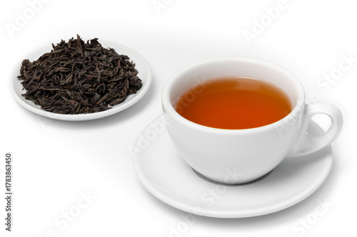 White cup of freshly brewed Ceylon Sabaragamuwa Orange Pekoe A tea on saucer with pile of dried black tea leaves on plate, isolated on white background