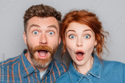 Surprised young man and woman with wide eyes and open mouths wearing denim shirts