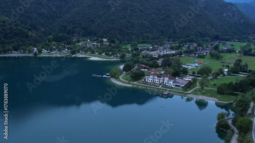 Drone view of Pieve di Ledro lakeside with village buildings and surrounding forested hills
