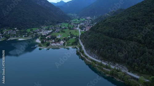 Aerial view of Pieve di Ledro village with lakeside road, forested hillside and mountain landscape
