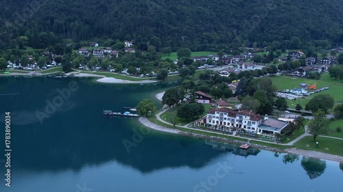 Aerial view of Pieve di Ledro lakeside with clear water, village buildings and mountain scenery
