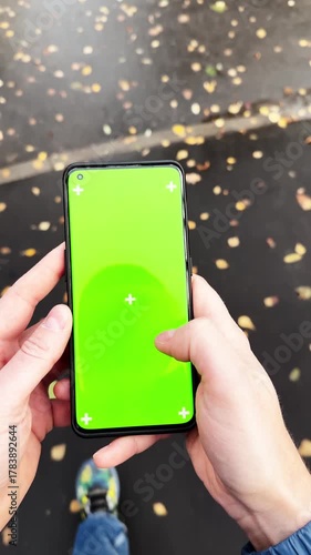 Close-up handheld view of person walking and using smartphone with green screen