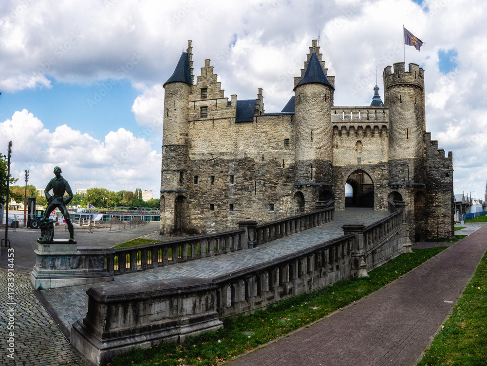 Obraz premium Historic castle with statue in Antwerpen under cloudy skies, showcasing architectural details and serene surroundings