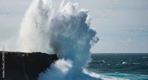Fototapeta Naklejka Na Ścianę i Meble -  Massive ocean wave crashing against a dark rocky coastline. Powerful sea spray exploding into the air. The raw force of nature and untamed energy. A concept of turbulence and impact