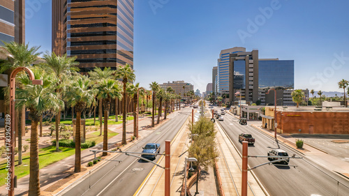 Vibrant street scene in downtown Phoenix, Arizona featuring palm trees lining a wide avenue with traffic and modern buildings. The sunny day creates a bright and energetic feel. Suitable for marketing