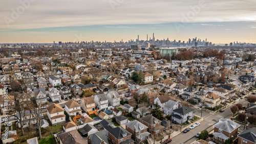 Panoramic aerial view of a residential neighborhood bathed in golden hour light. Houses line streets beneath a vibrant blue sky with wispy clouds. Urban landscape, suburban serenity, peaceful
