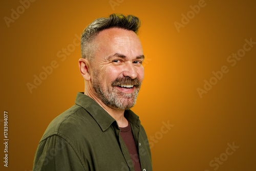 A cheerful man with a stylish haircut smiles broadly, showcasing his vibrant personality against a bright orange backdrop. The warm colors create a welcoming atmosphere filled with positivity