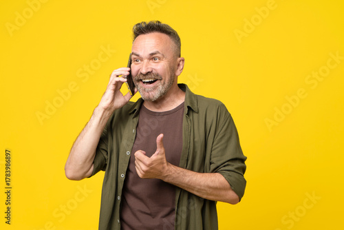Attractive senior 50 man having joyful happy conversation over smartphone, amazed smilling face, open mouth and hand thumb up gesture. man talking on mobile phone on yellow background