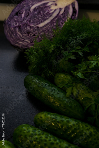Several cucumbers and herbs in close-up. Red cabbage is in the background