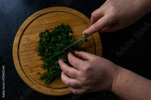 Someone is cutting herbs with a knife on a cutting board.