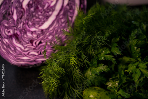 Several cucumbers and herbs in close-up. Red cabbage is in the background