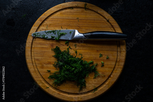 A kitchen board with a knife and chopped herbs on it