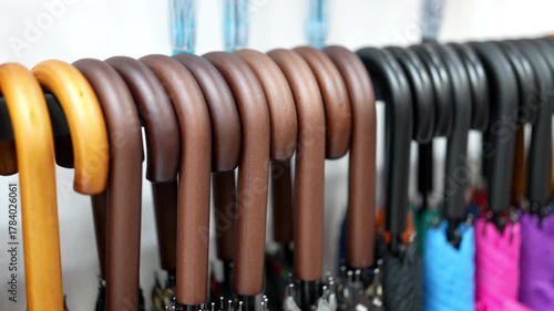 Umbrellas line the rack, waiting for a rainy day. Handles of wood in various shades curve gracefully above the folded canopy of blues, purples, greens, and blacks.