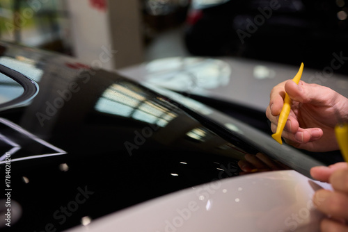Car hood restoration, Technician carefully cleans black car paint surface, Focused technician skillfully restores car surface with attention to detail and perfect finish