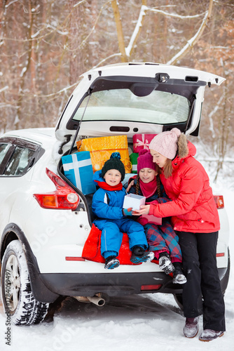 Smiling mom with her kids surrounded by holiday gift boxes in back of snowy car, enjoying magical winter forest day. Merry Christmas