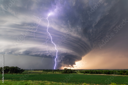 Supercell storm clouds and lightning strike over a field