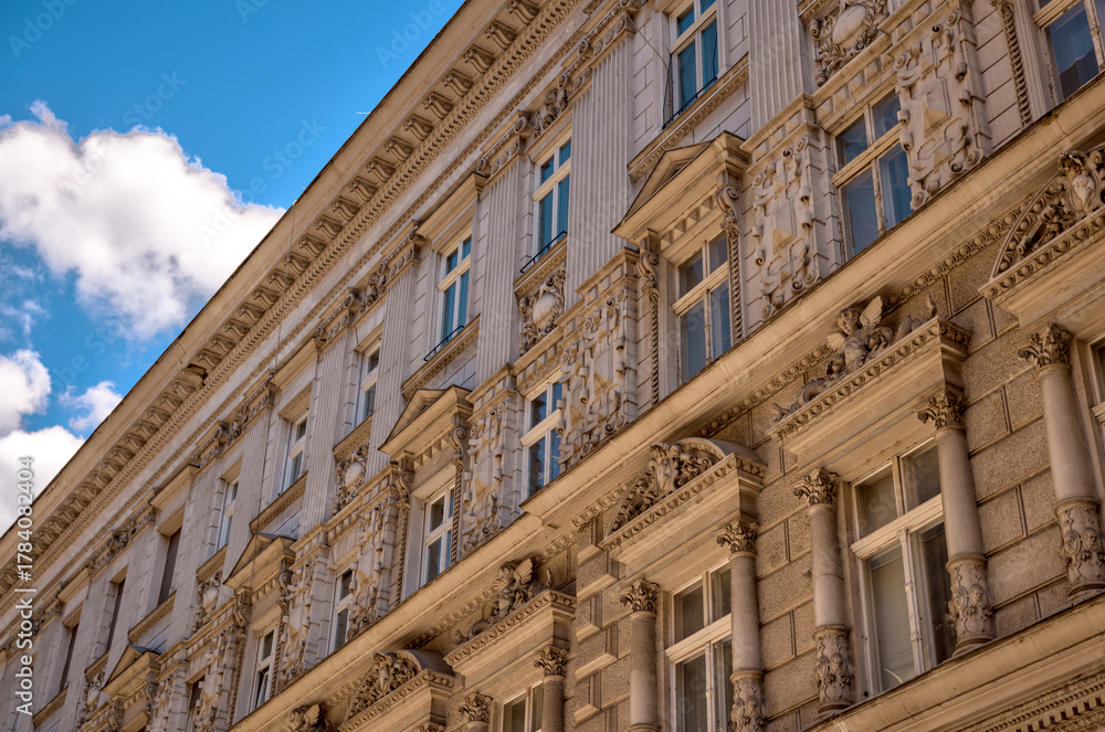 Fototapeta premium Budapest, Hungary – July 27, 2025: Colorful residential buildings with ornate balconies and street-level shops in downtown Pest, capturing the city’s architectural charm and everyday urban life.