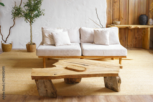 Bright cozy living room with light beige sofa, rustic wooden coffee table and light streaming through window. Home interior design in scandinavian style with warm tones and natural materials.