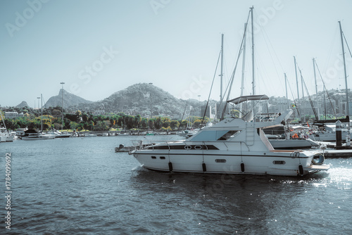 Luxury motor yacht docked at marina in Rio de Janeiro, Brazil, surrounded by sailboats and tropical hills under bright summer light, showcasing nautical lifestyle and leisure travel