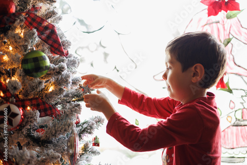 Young boy happily decorating a christmas tree by a window