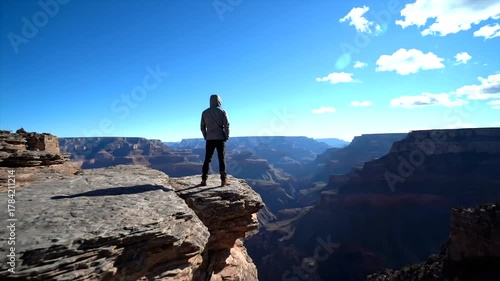 A person standing on the edge of a rocky cliff overlooking the vast Grand Canyon landscape
