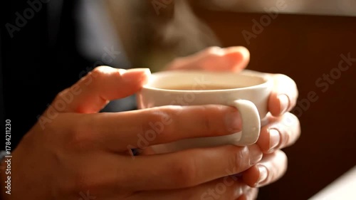 A person holding a steaming cup of coffee in a cozy café setting, with soft lighting