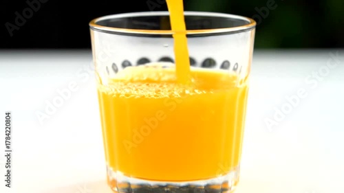 Fresh orange juice being poured into a clear glass on a bright, sunny table setting