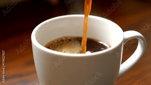 Hot beverage being poured into a white ceramic cup on a wooden table, with a cozy atmosphere