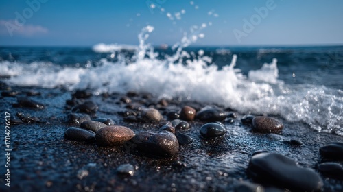 Fototapeta Naklejka Na Ścianę i Meble -  A rocky beach with pebbles and waves, under a clear blue sky with a few clouds.