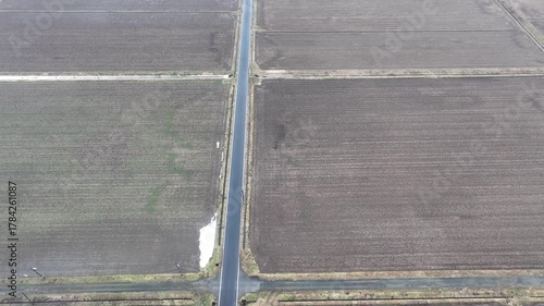 Drone footage rising over snowy rice fields toward sunlit mountains. The camera tilts up gradually, capturing morning sunlight illuminating distant peaks. Ideal for travel, nature, or meditation.