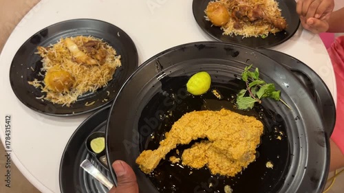 Spicy chicken chap served with biryani and mutton stew in black plate in Kolkata