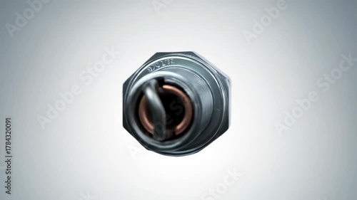 A detailed close-up of a metallic, threaded device with a white insulator, black cap, and a copper element. The device is placed against a gradient grey background