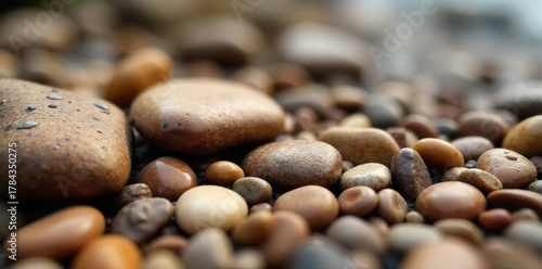 Pile of smooth, worn brown river stones and pebbles stacked and scattered. A close up, overhead view of smooth, rounded brown river stones and pebbles. Some are artfully stacked, while others are
