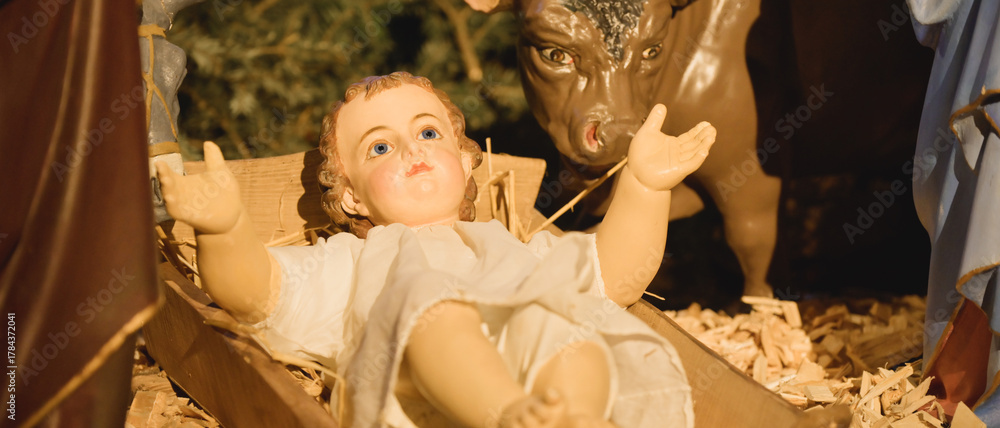 Obraz premium Gros plan sur le santon du petit Jésus qui lève les bras devant le bœuf dans la crèche de Noël, format bannière
