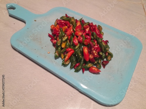 Large curly chilies that have been thinly sliced ​​with a sharp knife on a blue plastic chopping board
