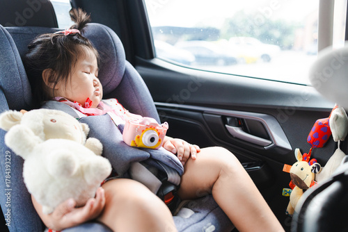 A cute little Asian girl is sleeping in a baby car seat inside a car during a travel trip,Cute little Asian girl is sleeping in car seat with teddy bear hugging. 