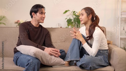 Asian adult couple enjoys lively genuine conversation at home in their cozy modern living room sharing happy moments discussing life together