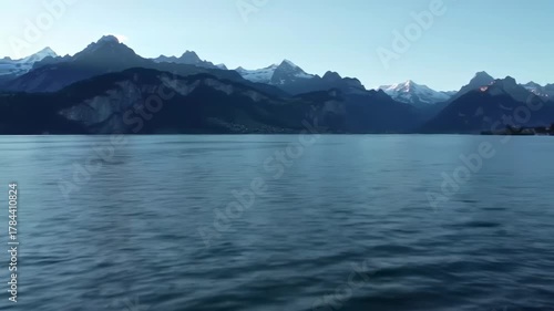 Wallpaper Mural A serene landscape showing a calm body of water reflecting the majestic, snow-capped mountains in the background under a pale, clear sky Torontodigital.ca