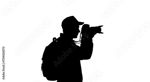 Silhouette of a photographer wearing a cap and backpack, holding a camera and taking a picture against a white background.