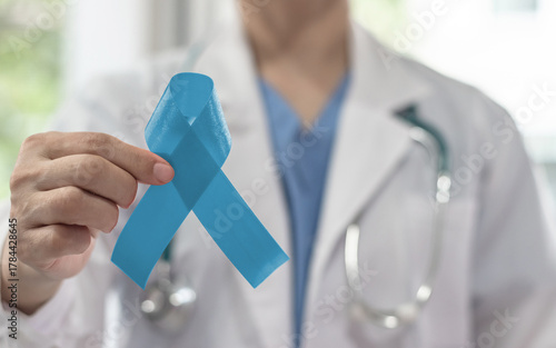 Prostate cancer blue awareness ribbon for men health and male mental health care concept with pale light blue bow color on medical doctor's hand in hospital background