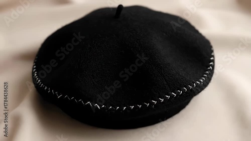 Close Up of a Black Beret with Silver Stitching on Beige Fabric Surface Flatlay Style High Angle Fashionable Headwear Accessory
