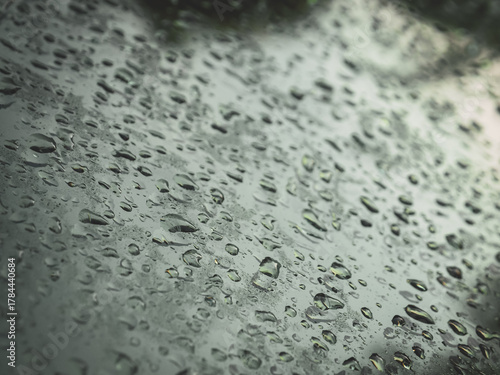 Close-up view of raindrops on a car window during a rainy day. Water droplets create a soft abstract pattern with reflections and blurred lights outside. Perfect for backgrounds, weather concepts