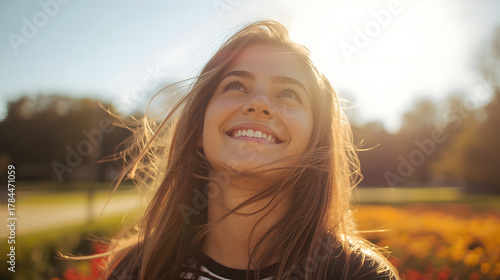 young woman smiling brightly with sparkling eyes, looking up at a clear sunny sky