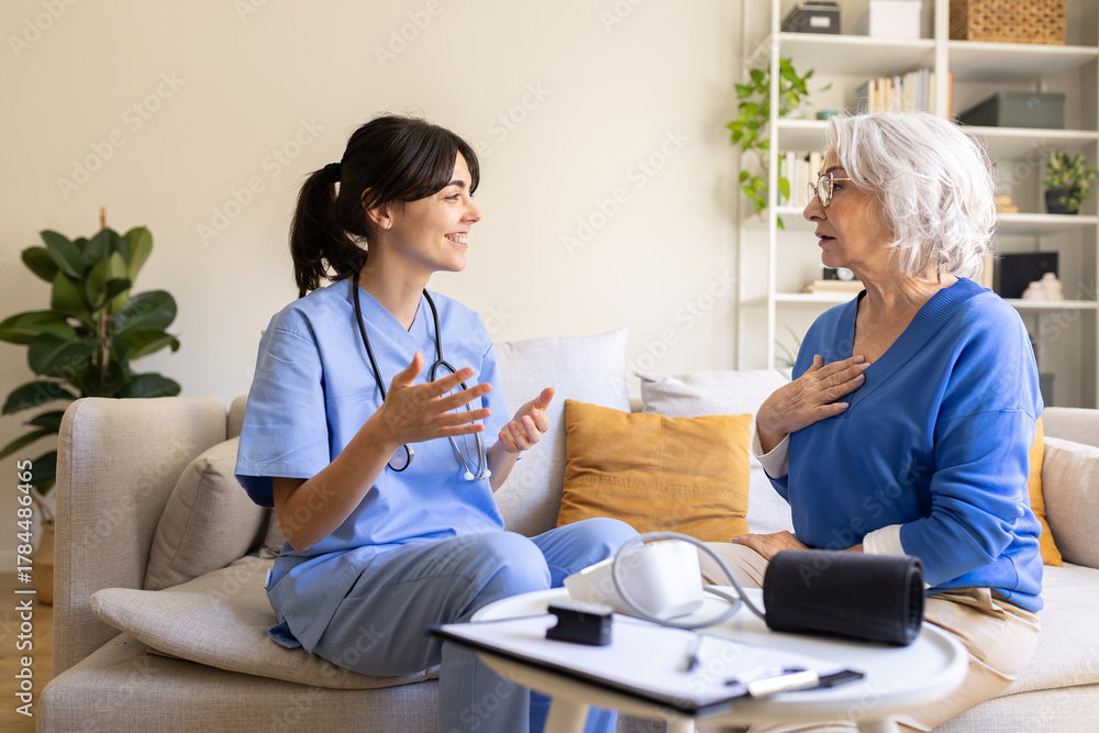 Fototapeta premium Female doctor visiting elderly woman at home discussing symptoms