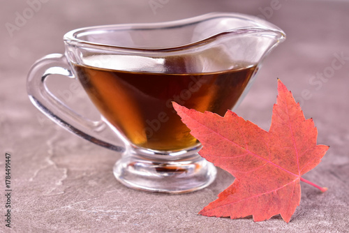 Maple syrup in a glass sauceboat on a gray background. Close-up.
