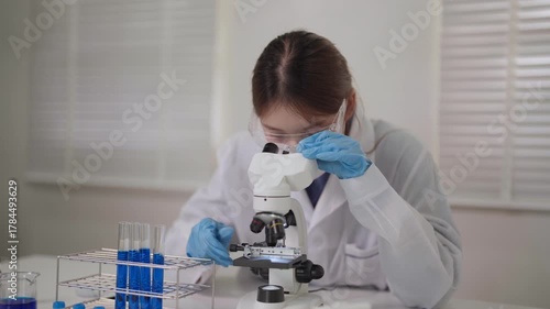 Asian adult woman scientist conduct scientific research experiment in laboratory focused microscope examination chemistry biology medical discovery healthcare